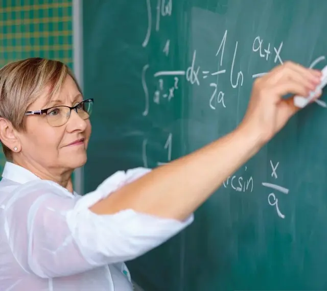 Nauczyciel początkujący pisze kredą wzory matematyczne na tablicy.