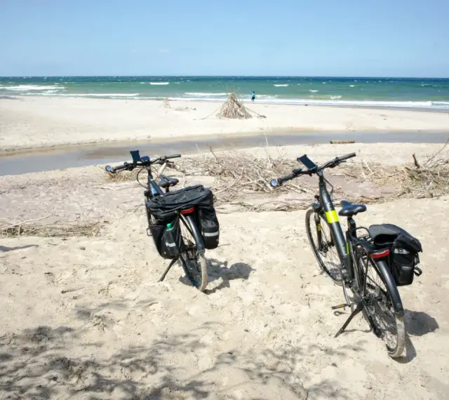 Dwa rowery z sakwami na piaszczystej plaży, gotowe do odkrywania tras rowerowych nad morzem.