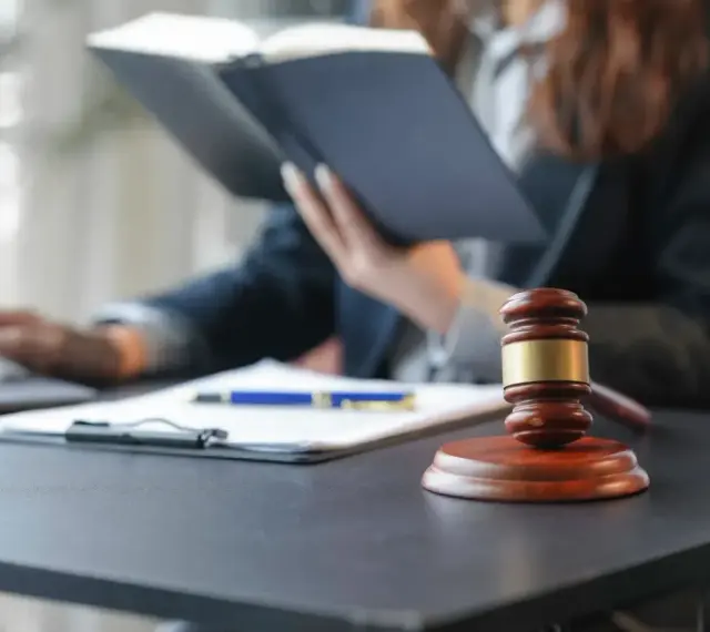 Sądowy młotek i dokumenty na biurku. Prawnik w tle studiuje akta, zastanawiając się, czy radca prawny może być obrońcą.