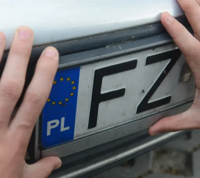 Dwie dłonie trzymają polską tablicę rejestracyjną z literami FZ.