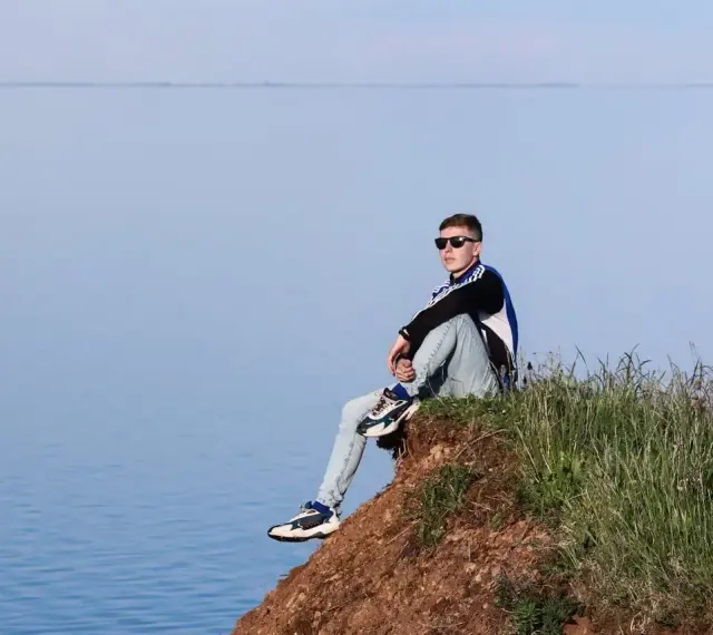 Chłopak siedzi na skarpie nad jeziorem, zastanawiając się, gdzie na wakacje z nastolatkiem w Polsce.