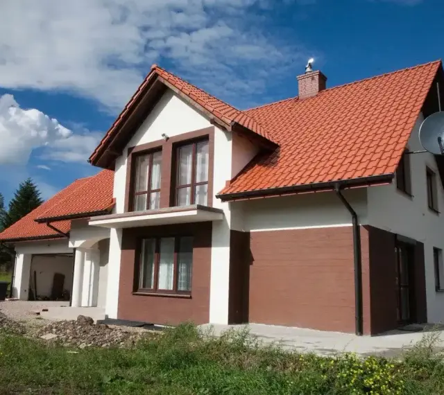 Jaki kolor elewacji do czerwonego dachu? Biała elewacja z brązowymi akcentami, jak na tym domu, wygląda stylowo.