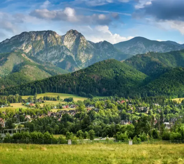Malowniczy widok na Tatry z Jaszczurówki, gdzie liczne atrakcje czekają na turystów. Zielone wzgórza i tradycyjna zabudowa tworzą sielski krajobraz.