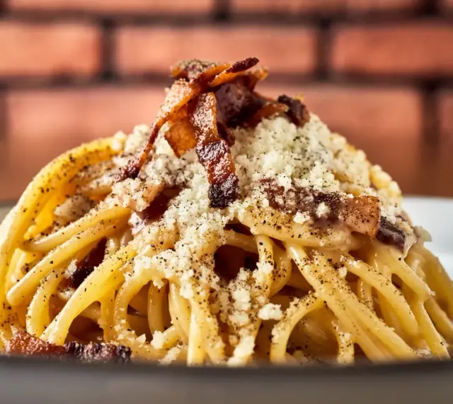 Pyszny makaron włoski carbonara z chrupiącym boczkiem i parmezanem, posypany świeżo mielonym pieprzem.