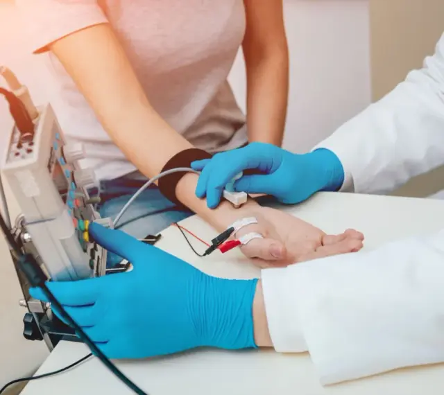 Badanie EMG, czyli elektromiografia, to badanie oceniające funkcję nerwów i mięśni. Lekarz z niebieskimi rękawiczkami podłącza elektrody do ręki pacjentki.