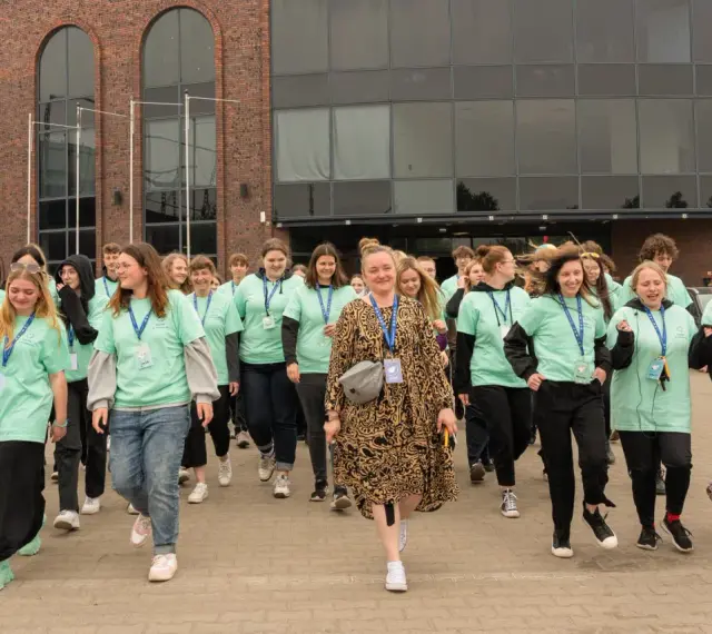 Grupa młodych ludzi w zielonych koszulkach z napisem "Szkoła w chmurze" idzie przed budynkiem.