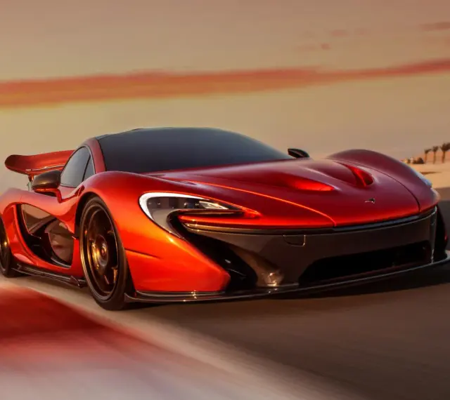 Czerwony McLaren P1 pędzi po pustynnej drodze o zachodzie słońca.
