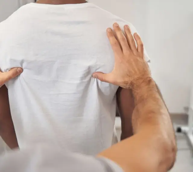 Fizjoterapeuta bada plecy pacjenta, oceniając kręgosłup piersiowy pod kątem objawów neurologicznych.