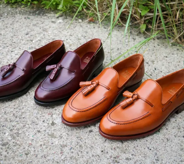 Eleganckie, skórzane loufersy z chwostami w kolorze koniaku i burgundu, ułożone na betonowej nawierzchni.