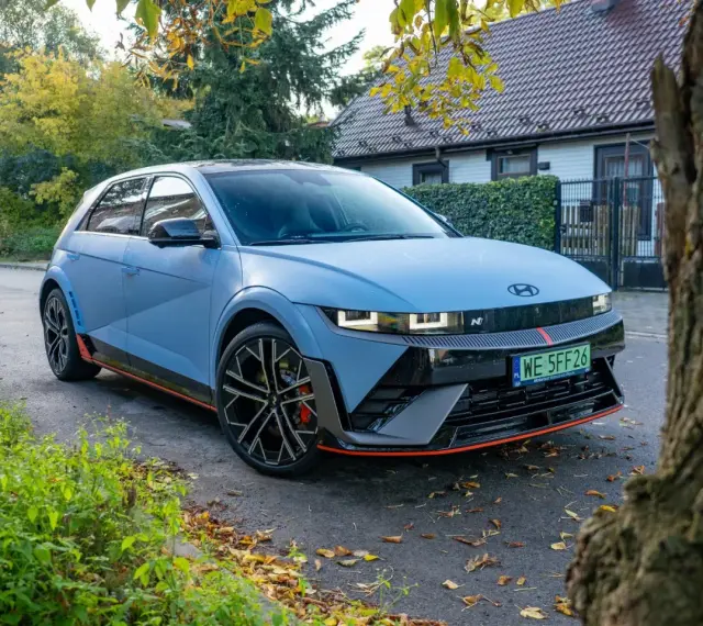 Niebieski Hyundai Ioniq 5 N z czerwonymi akcentami stoi na tle domu i drzew.