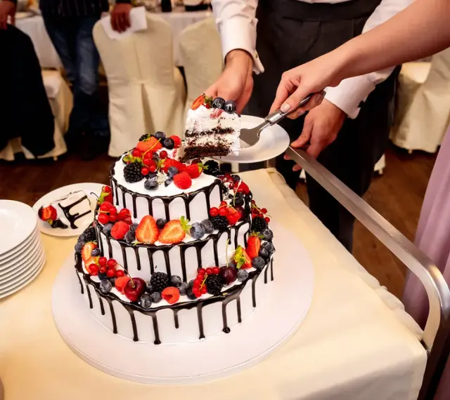 Piękne torty weselne z owocami, ozdobione czekoladą i świeżymi jagodami, malinami i truskawkami. Para kroi pierwszy kawałek.