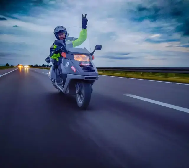 Karta motorowerowa w akcji! Kierowca w kasku i kamizelce odblaskowej pozdrawia, jadąc skuterem po autostradzie.