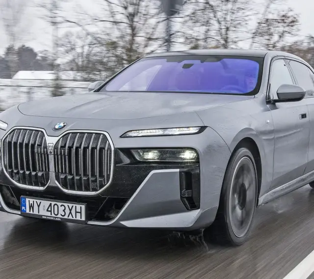Szary BMW Serii 7 w ruchu, z widocznym grillem i reflektorami. Sprawdź aktualną bmw 7 cena.