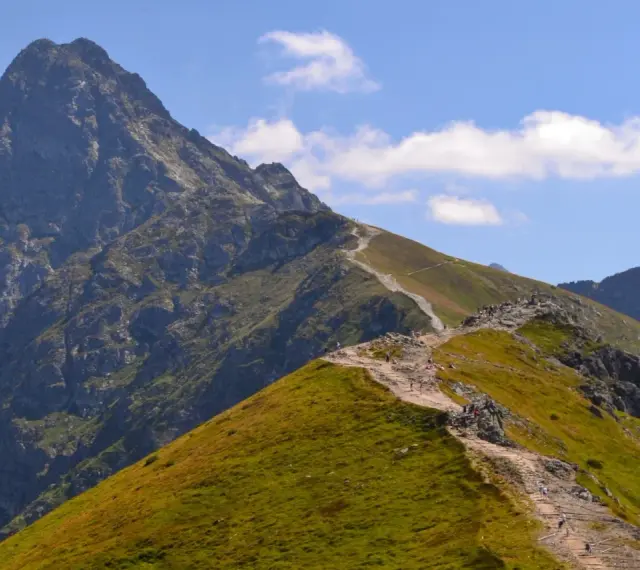 Kamienista ścieżka wije się po zielonych zboczach, prowadząc turystów ku majestatycznym tatry zachodnie szczyty.