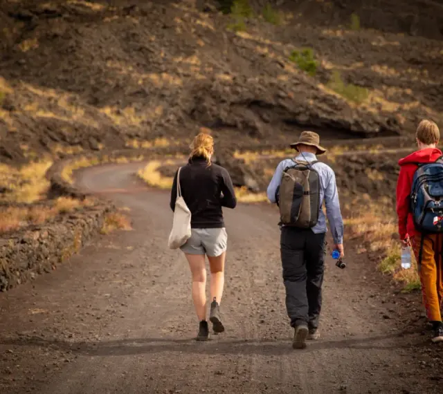 Trzy osoby wędrują po wulkanicznym krajobrazie Sycylii. Styczeń na wyspie oferuje przyjemną temperaturę do trekkingu.