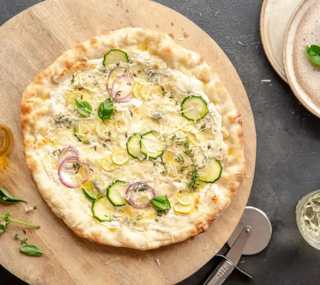 Pyszna pizza bianca z cukinią, cebulą i cytryną, posypana parmezanem i ziołami. Idealna na letni wieczór.