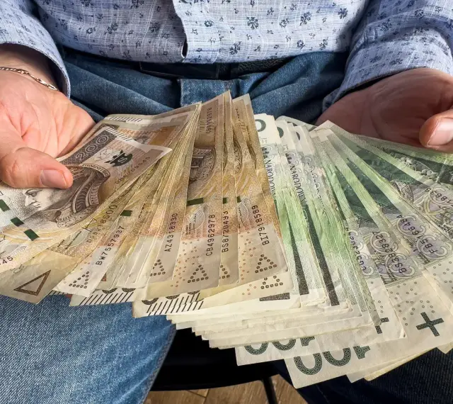 Ręce trzymające stos banknotów, w tym 1000 plus złotych. Widać portret Kopernika na jednym z banknotów.