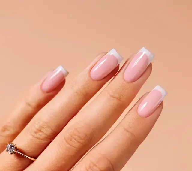 Dłonie z idealnym manicure french na paznokciach. Delikatny róż i biel tworzą klasyczny french na paznokciach, podkreślony subtelnym pierścionkiem.