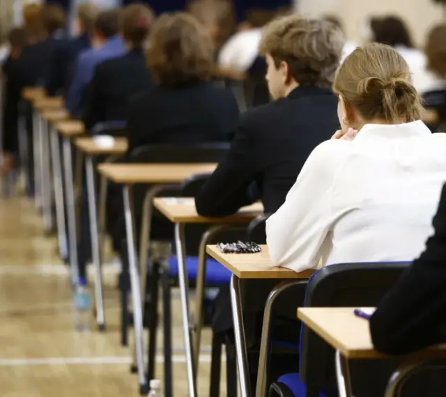 Uczniowie siedzą w rzędach przy ławkach, skupieni na rozwiązywaniu pytań maturalnych.