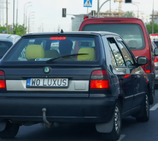 Czarny samochód z indywidualnymi tablicami rejestracyjnymi "WO LUXUS" w korku ulicznym.