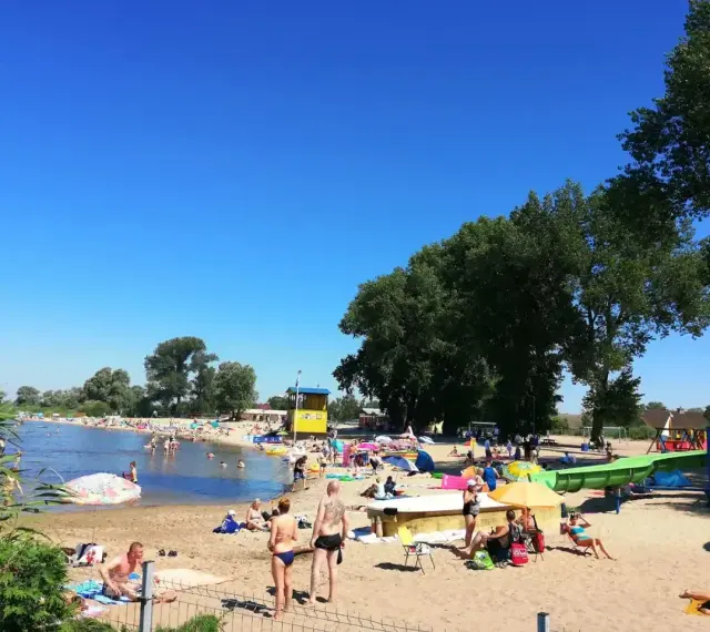 Słoneczny dzień na plaży, ludzie odpoczywają nad wodą. Zastanawiasz się, ile kilometrów jest ze Szczecina nad morze? To idealne miejsce na relaks przed podróżą.