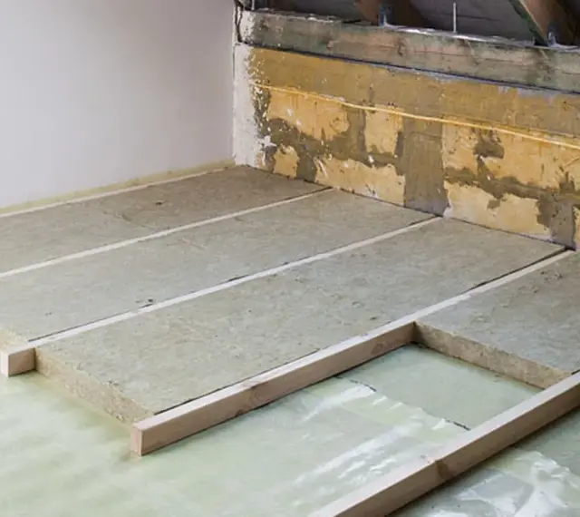 Ocieplenie stropu betonowego w trakcie prac. Płyty izolacyjne ułożone na folii, podparte drewnianymi legarami.