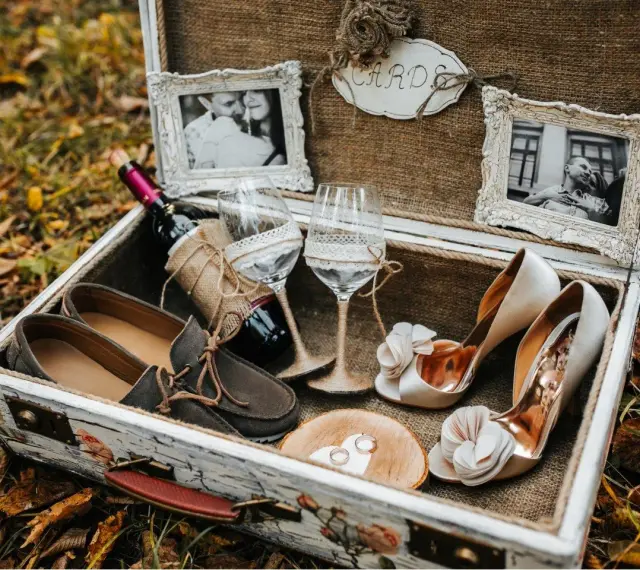 Elegancki prezent na ślub cywilny bez wesela: buty, wino, kieliszki, obrączki i zdjęcia pary w ozdobnej skrzyni.