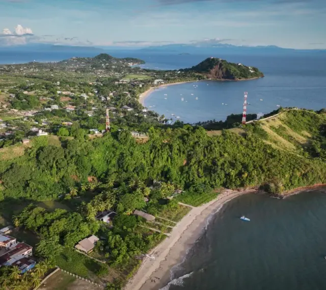 Malownicze miasto na Madagaskarze z zielonymi wzgórzami, plażą i zatoką pełną łodzi. W oddali góry.