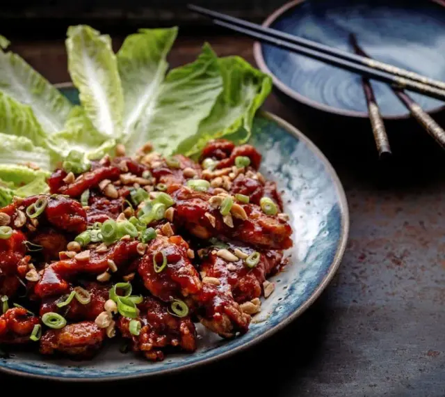 En tallrik med krispiga, glaserade kycklingvingar, toppade med hackade jordnötter och salladslök. Serveras med krispiga salladsblad. En utsökt koreansk matupplevelse.