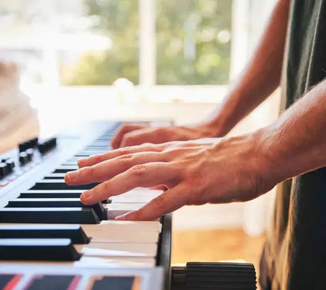 Dłonie grające na keyboardzie. To instrument muzyczny, który pozwala tworzyć melodie.