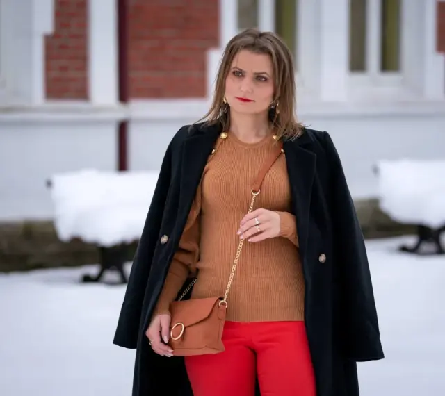 Elegancka stylizacja: co ubrać do czerwonej spódnicy? Brązowy sweter, czarny płaszcz i karmelowa torebka tworzą stylowy zestaw.