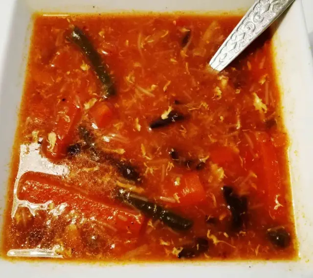 Aksamitna zupa ostro kwaśna z kawałkami warzyw i jajka, podana w białej misce.