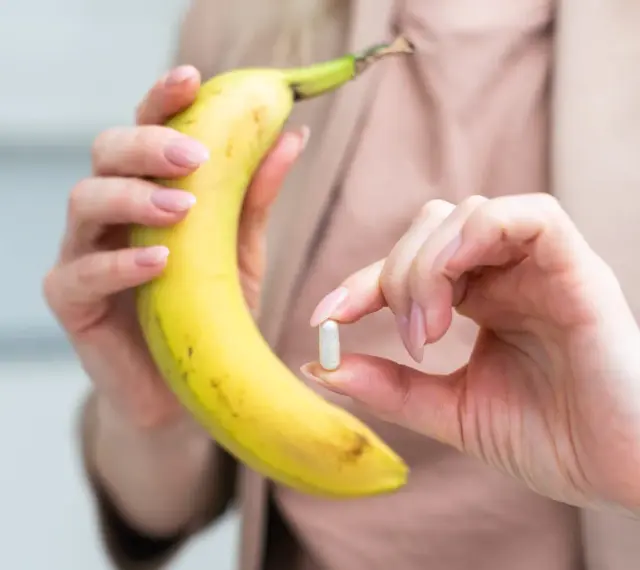 Kobieta trzyma banana i tabletkę, zastanawiając się, ile potasu dziennie powinna przyjmować.