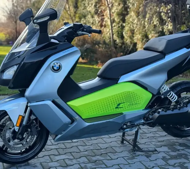 Srebrno-czarny skuter elektryczny BMW C Evolution z zielonym akcentem i napisem "C Evolution" na boku, stojący na chodniku.