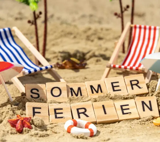 Strandkörbchen, Palmen und die Worte "Sommerferien" im Sand. Perfekt für die Sommerferien in Brandenburg!