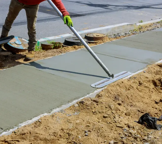 Robotnik wygładza świeży beton B25 na chodniku. Właściwe proporcje składników zapewniają trwałość nawierzchni.