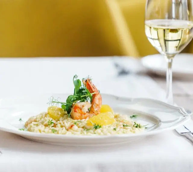 En elegant tallrik med saffransrisotto, toppad med en saftig räka och citrusklyftor. Ett glas vitt vin till saffransrisotto fulländar denna läckra måltid.