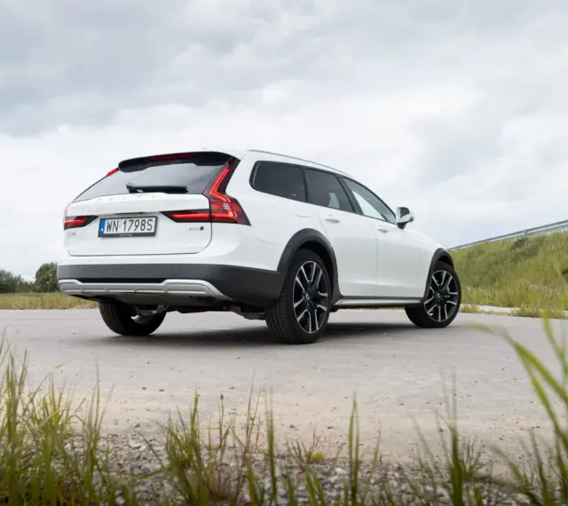 Białe Volvo Cross Country na tle pochmurnego nieba i zielonych wzgórz.