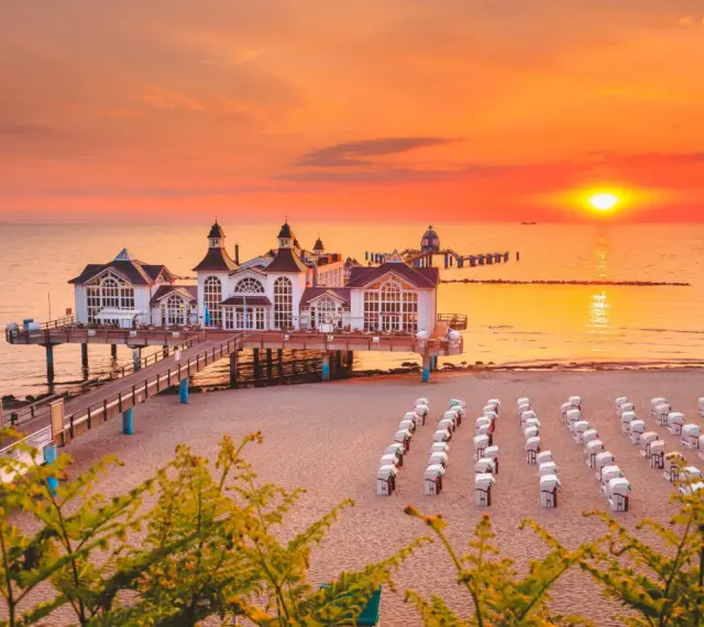 Zachód słońca nad molo w Sellin, na Rugii, największej wyspie Niemiec. Puste kosze plażowe czekają na gości.
