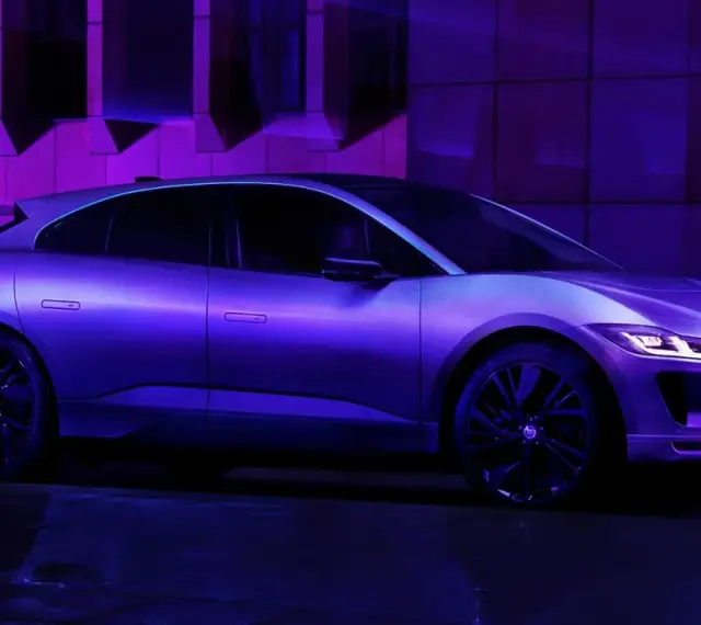 Jaguar I-Pace w fioletowym świetle, zaparkowany na mokrej nawierzchni.