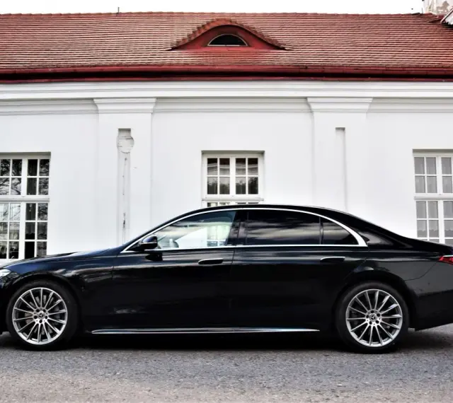 Elegancki, czarny Mercedes S500 lśni na tle białej, zabytkowej fasady z czerwonym dachem.