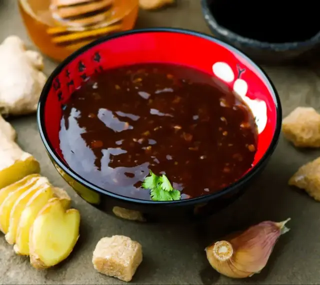 Miseczka z aromatycznym sosem teriyaki, obok świeży imbir, czosnek i brązowy cukier.