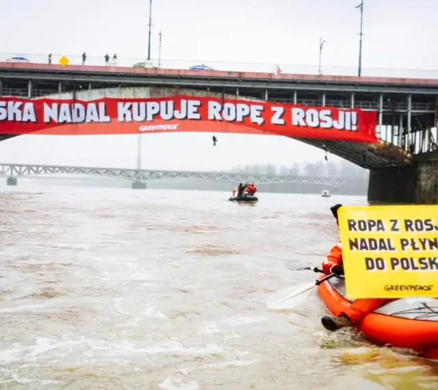 Na moście Poniatowskiego wisi czerwony baner "Polska nadal kupuje ropę z Rosji!". Kajakarz Greenpeace na Wiśle trzyma żółtą tablicę "Ropa z Rosji nadal płynie do Polski".