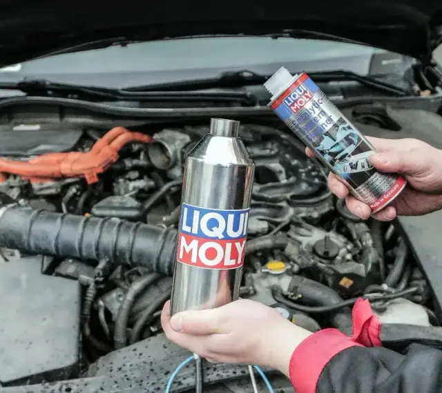 Dwie ręce trzymają produkty Liqui Moly, jeden metalowy, drugi w sprayu, gotowe do czyszczenia katalizatora w silniku samochodu.