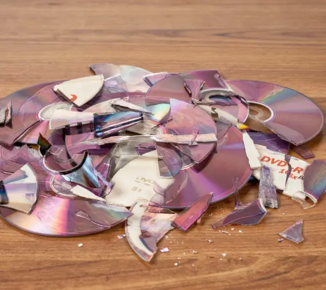 Stos zniszczonych płyt DVD i CD na drewnianym blacie. Czy płyty CD to elektrośmieci? Pytanie o ich utylizację nabiera sensu.