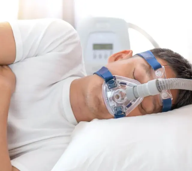 Mężczyzna śpi z maską CPAP, która pomaga mu oddychać podczas bezdechu sennego.