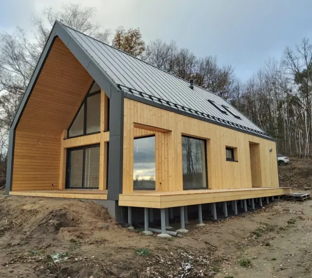 Nowoczesny dom 70m2 z drewnianą elewacją i dużymi oknami, otoczony lasem.