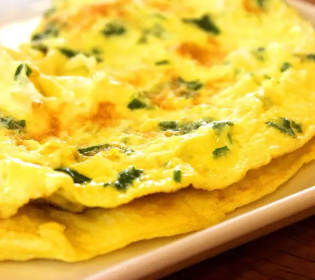 Złożony omlet z zielonymi ziołami na białym talerzu.