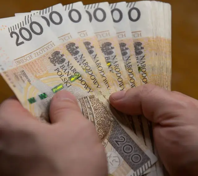 Dłonie trzymają stos banknotów po 200 zł. Czy to wystarczy, by poznać, ile wynosi najniższa krajowa netto?