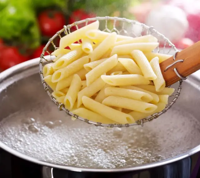Penne w cedzaku nad garnkiem z wrzącą wodą. Prosty sposób, jak ugotować makaron do ulubionego sosu.